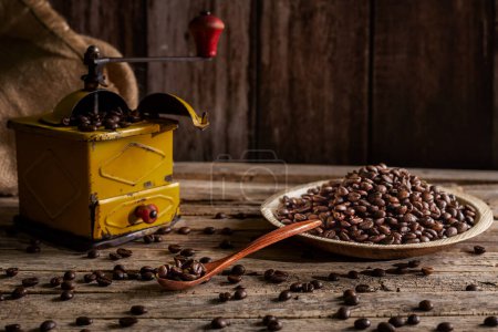 Foto de Granos de café tostados en un plato y en una cuchara de madera junto a un molinillo a la antigua para moler café. - Imagen libre de derechos