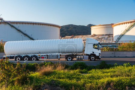 Téléchargez les photos : Camion citerne pour le transport de gaz cryogéniques dangereux circulant le long d'une route avec de grands dépôts d'une raffinerie. - en image libre de droit