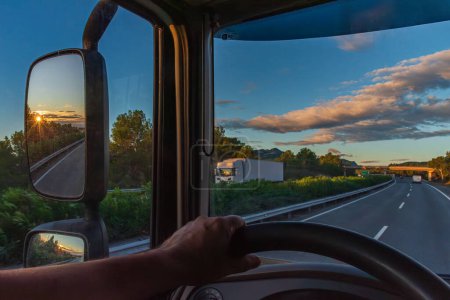 Foto de Vista desde el asiento del conductor de un camión de una carretera al amanecer y el sol reflejado en el espejo retrovisor. - Imagen libre de derechos
