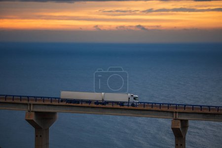 Foto de Mega-camión remolque que conduce sobre un puente con el mar y el cielo del amanecer en el horizonte. - Imagen libre de derechos