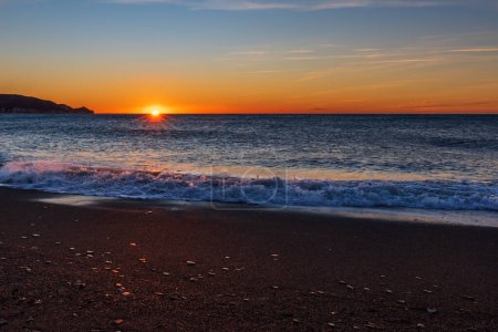 Foto de Playa Poniente en Motril, Granada, con el sol saliendo al amanecer sobre el horizonte del mar Mediterráneo. - Imagen libre de derechos