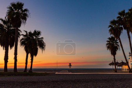 Photo for Sunrise on Poniente beach, Motril, Granada, with palm trees, a beach bar and a watchtower for bathers. - Royalty Free Image