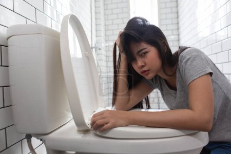 Photo for Woman looking at camera drunk hangover puke in toilet bowl. Female have abdominal pain, nausea, dizziness, nausea, vomit due to food poisoning. - Royalty Free Image