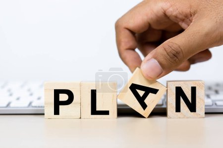 Planning concept. Wooden cube with Text PLAN on table keyboard computer background. Good leader must have a strategic plan. Hand picking character A.