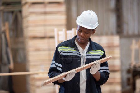 Foto de Hombre americano africano con uniforme de seguridad y sombrero duro inspección de calidad de trabajo de productos de madera en el taller de fabricación de madera. carpintero masculino trabajador madera almacén industria. - Imagen libre de derechos