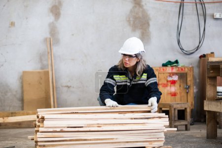 Foto de Mujer con uniforme de seguridad y sombrero duro inspección de calidad de trabajo de productos de madera en el taller de fabricación de madera. mujer carpintero trabajador madera almacén industria. - Imagen libre de derechos