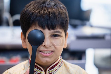 Foto de Niño indio examinando la visión chequeo visión clarividencia examina hospital oftalmológico. doctor usando oclusor para la prueba oftalmológica del ojo para el muchacho indio. - Imagen libre de derechos