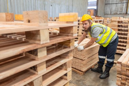 Téléchargez les photos : Homme portant un uniforme de sécurité et un casque jaune qui vérifie la qualité des produits en bois lors de la fabrication en atelier de bois. Homme charpentier ouvrier bois entrepôt industrie. - en image libre de droit