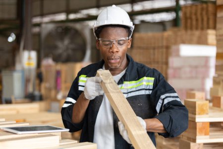 Téléchargez les photos : Homme portant un uniforme de sécurité et un casque jaune qui vérifie la qualité des produits en bois lors de la fabrication en atelier de bois. Homme charpentier ouvrier bois entrepôt industrie. - en image libre de droit