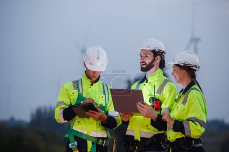 Team engineer wearing safety uniform holding laptop discussed plan about renewable energy at station energy power wind. technology protect environment reduce global warming problems.