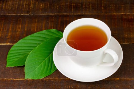 Mitragyna Speciosa Korth o té kratom en taza blanca con hoja verde sobre fondo rústico de madera.