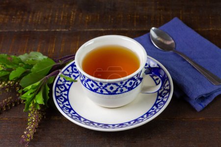 Tulsi o té de albahaca sagrada en taza blanca con hoja de tul fresco sobre fondo de madera. Medicina ayurvédica en India.