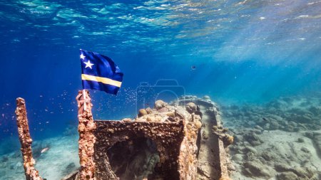Téléchargez les photos : Épave de navire "Tugboat" dans les eaux peu profondes du récif corallien dans la mer des Caraïbes avec drapeau Curaçao, vue sur la surface et les rayons de soleil - en image libre de droit