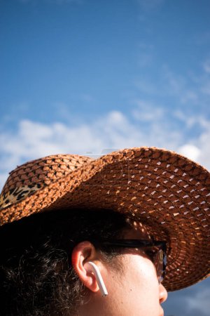 Photo for Woman wearing a wicker hat and using an earphone on sunny day - Royalty Free Image
