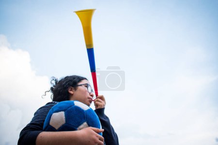 Téléchargez les photos : Femme tenant le ballon de football bleu et utilisant vuvuzela pour soutenir l'équipe dans la journée nuageuse - en image libre de droit