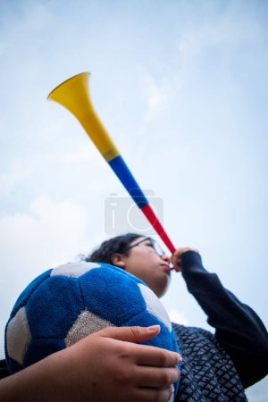 Téléchargez les photos : Femme tenant le ballon de football bleu et utilisant vuvuzela pour soutenir l'équipe dans la journée nuageuse - en image libre de droit