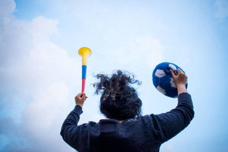 Téléchargez les photos : Femme célébrant avec vuvuzelaand ballon de football dans ses mains dans la journée nuageuse - en image libre de droit