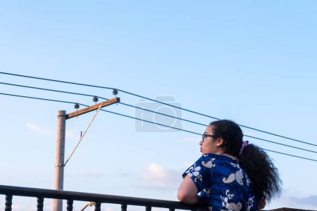 Mujer de pie y vestido azul en la terraza en la ciudad latina con una torre eléctrica en verano 