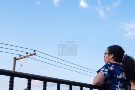 Frau steht und trägt blaues Kleid auf einer Terrasse in der lateinischen Stadt mit einem elektrischen Turm im Sommer 
