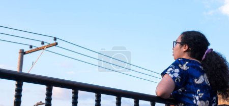 Mujer de pie y vestido azul en la terraza en la ciudad latina con una torre eléctrica en verano 