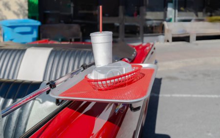 Photo for Food tray on an antique red convertible vintage car with a styrofoam drink cup red straw and styrofoam hotdog holder. Selective focus on food tray and contents. - Royalty Free Image