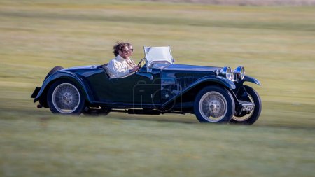 Photo for Old Warden, UK - 2nd October 2022: Vintage car 1933 Riley Nine Lynx tourer  being driven at speed along a grass runway - Royalty Free Image