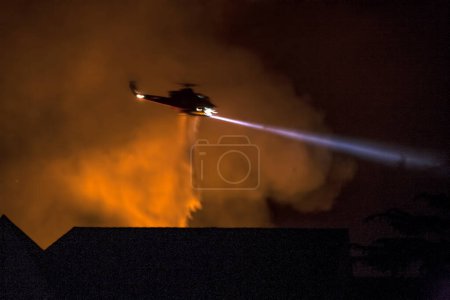A fire fighting  helicopter drops water over a neighborhood experiencing a brush fire in Los Angeles