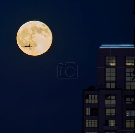 An airplane approaches San Diego International Airport during a full moon.