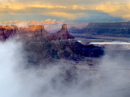 A passing rainstorm leaves residual clouds and fog as the sun penetrates the red rock landscape at Dead Horse Point State Park, Utah