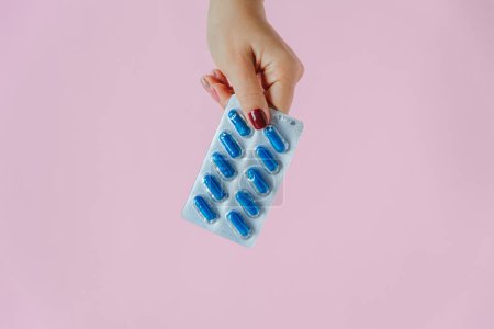 Photo for Women hand holds blue capsules in blister on pink background. Pharma and medicine concept. Top view - Royalty Free Image