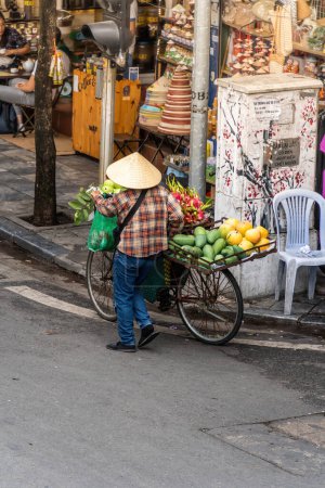 Foto de Hanoi, Vietnam - 08 de mayo de 2023: Personas, vendedores, bicicletas y conductores de ciclomotores que llevan al turista a una calle concurrida y bulliciosa en el casco antiguo de Hanoi, en el norte de Vietnam. Famoso destino de Vietnam - Imagen libre de derechos