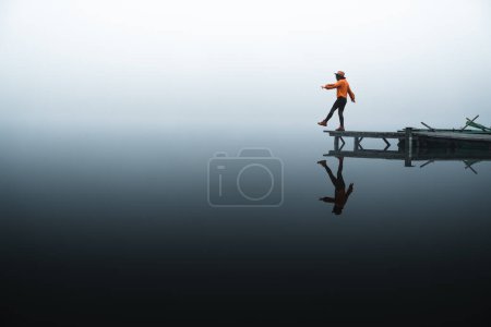 Téléchargez les photos : Side view of fashioned young woman sitting on wooden dock looking at view on a misty morning. - en image libre de droit