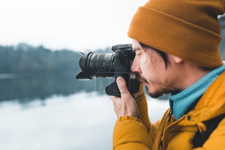 Photo for Outdoor photographer taking landscape photos using digital camera. Side view of man using dsrl against lake and forest - Royalty Free Image
