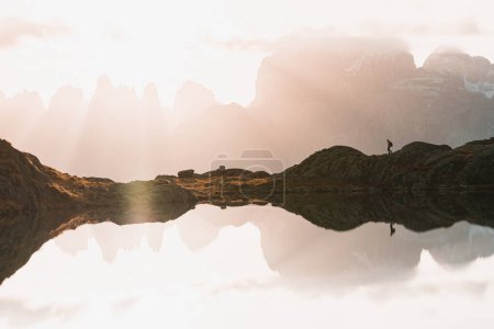 Téléchargez les photos : Panoramic view of hiker with alpine mountain lake reflection during sunrise. Climber man walks alone with Italian Alps mountains in background while it is reflected in the Lago Nero, Valgoglio, Italy - en image libre de droit