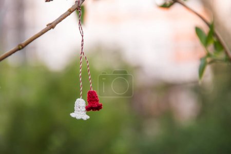 Symbol of the first day of spring Martisor. Tradition of giving red and white souvenir. At the end of March, Martisor is hung on a tree branch and wishes are made. Green natural background, Copy Space