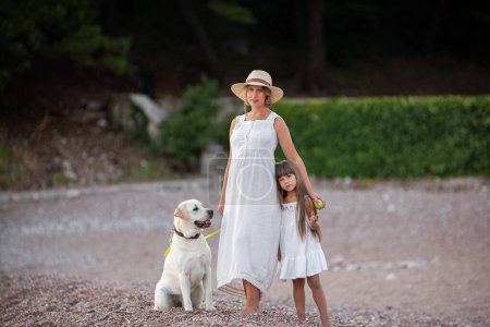 Photo for Pregnant mother with little daughter are walking along the sand of the beach near the sea with golden retriever. Millennial woman holds dog on leash, girl by the hand. Concept of traveling with pets - Royalty Free Image