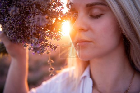 Photo for Close-up portrait of young woman with bouquet of purple lavender in front of face. Blonde millennial girl with clean skin without makeup in rays of sunset. Allergy concept. Aroma oils natural perfumes - Royalty Free Image