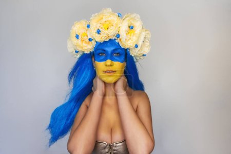 Portrait en gros plan créatif de la jeune patriote ukrainienne au visage jaune bleu, couronne de fleurs sur la tête sur fond gris isolé. Jour du drapeau, Jour de l'indépendance en Ukraine. Espace de copie