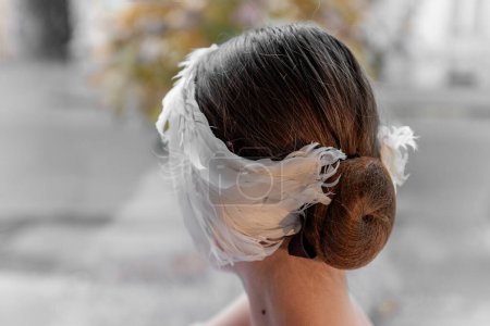 Nahaufnahme eines einzigartigen Stirnband-Tiara aus weißen Federn, das um einen Ballerina-MädchenhaarDutt gewickelt ist und Tradition mit modernem Stil verbindet. Ballettfrisur