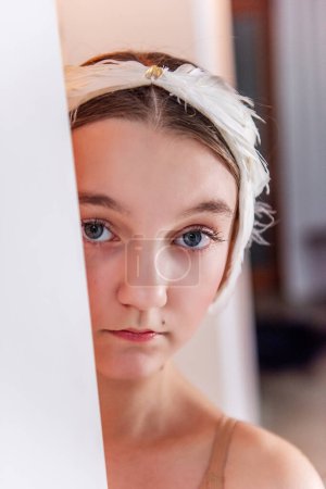 Close up portrait of ballerina with white tiara. Young dancer peeks from behind a wall, eyes expressing the anticipation and focus before a ballet performance.