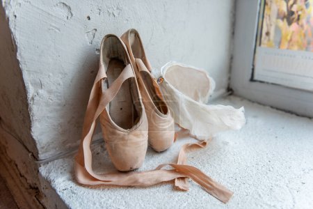 Téléchargez les photos : Chaussures pointes bien utilisées avec rubans, diadème en plumes blanches à côté de la fenêtre, racontant l'histoire de la dédicace et l'art gracieux du ballet. - en image libre de droit