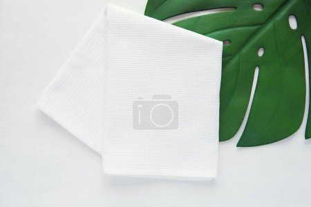 Foto de White waffle fabric kitchen towel mockup, folded blank cotton tea towel for design presentation, minimal composition with monstera leaf. - Imagen libre de derechos