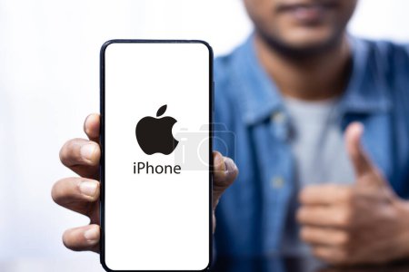 Foto de Primer plano de una pantalla de teléfono inteligente con el logotipo del iphone sostenido en la mano por un macho sonriente indio - Imagen libre de derechos