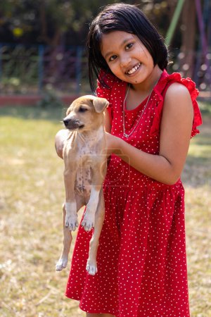 Photo for An Indian girl child playing with a cute brown puppy on field - Royalty Free Image
