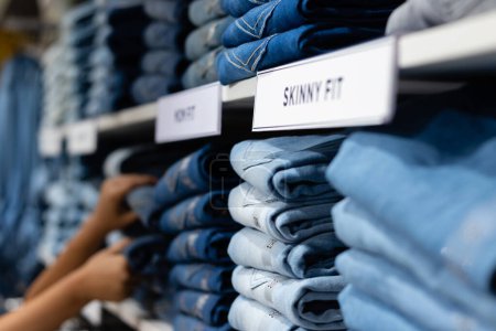 Photo for Selective focus on denim jeans arranged in racks and human hand in a shopping mall - Royalty Free Image