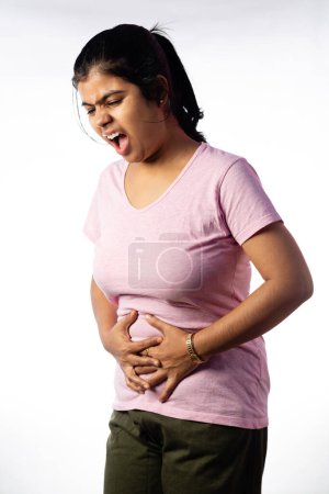 Una mujer india sosteniendo su abdomen por dolor mostrando expresión dolorosa sobre fondo blanco