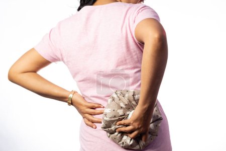 An Indian woman using hot water bag for back pain relief white background