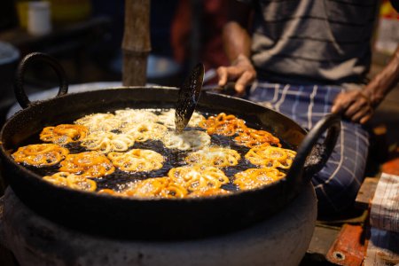 An Indian shopkeeper at mela or rural fair frying sweets jalebi in oil