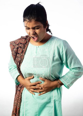 Una mujer india sosteniendo su abdomen por dolor mostrando expresión dolorosa sobre fondo blanco