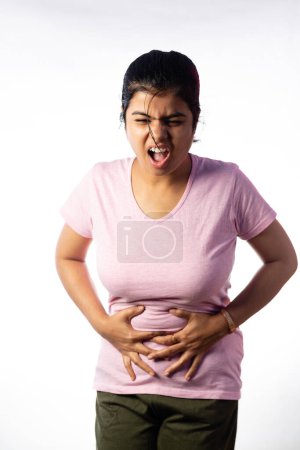 An Indian woman holding her abdomen for pain showing painful expression on white background
